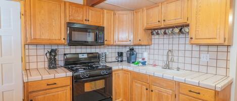 A kitchen with wooden cabinets, a black stove, a microwave, and a tiled backsplash.