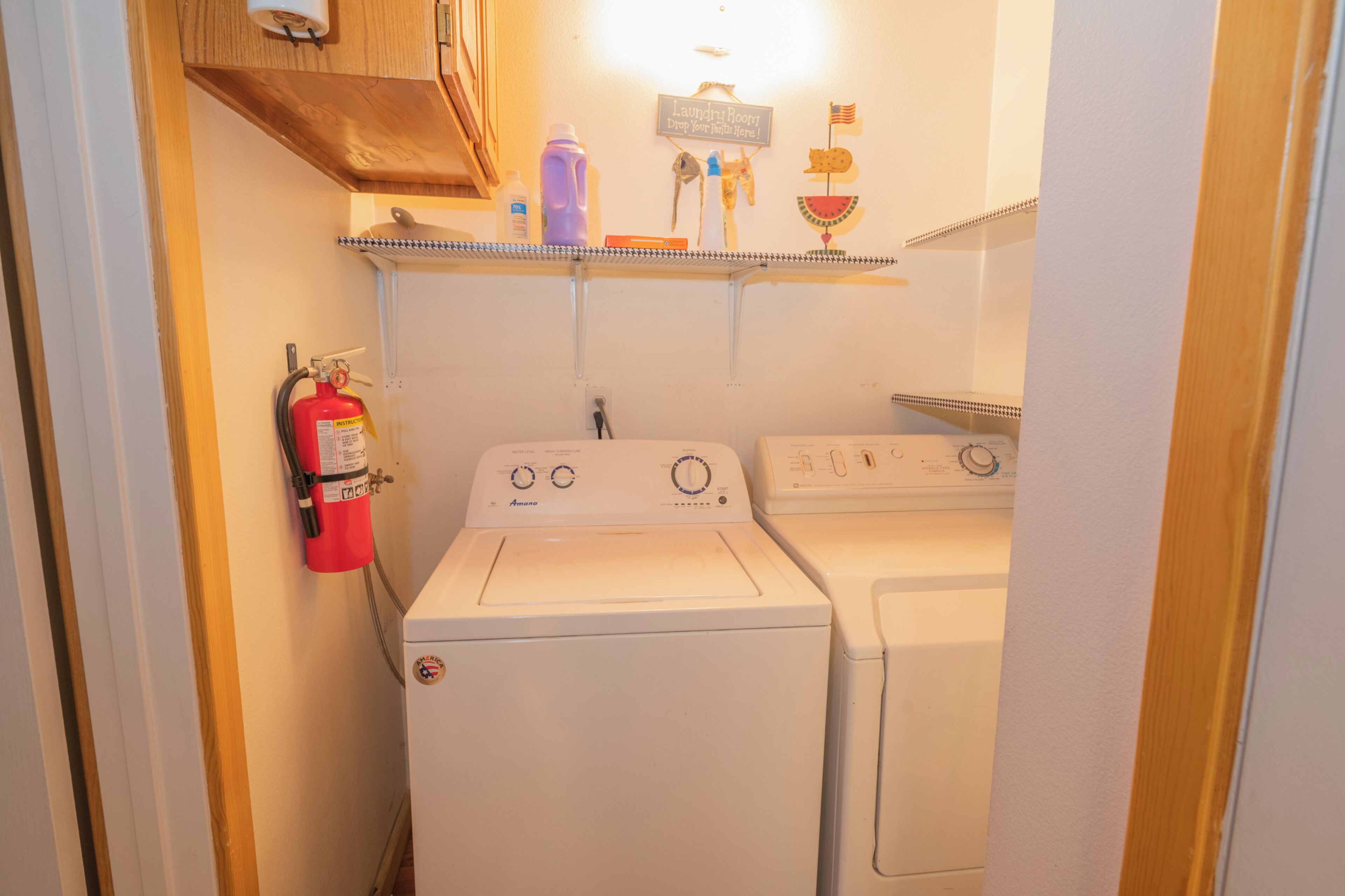 Une buanderie équipée d’un lave-linge et d’un sèche-linge à chargement frontal, d’un extincteur et d’une étagère contenant des produits de lessive.