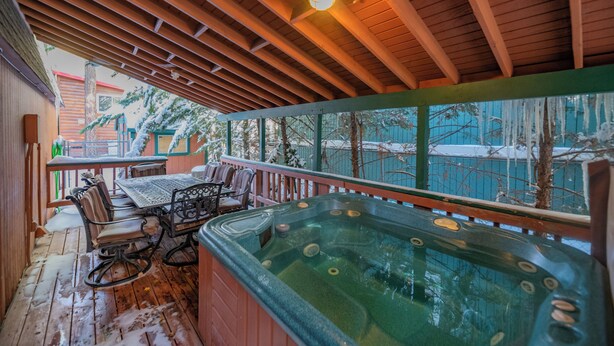 Una terraza de madera con un jacuzzi, zona de estar y vistas a árboles y un edificio.