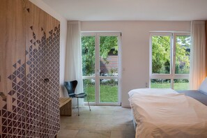 Un dormitorio con cama, una silla, un armario y un ventanal corredera que da a un jardín.