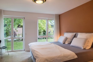 Une chambre à coucher avec un lit, des oreillers, une chaise et de grandes fenêtres.