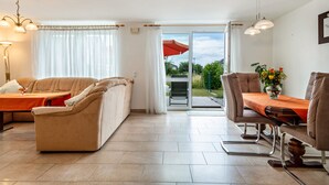 A living room with a sofa, a dining table with chairs, a large window with curtains, and a sliding glass door leading outside. - Holiday Home 'Storchennest' with Private Terrace, Private Garden and Wi-Fi (Markdorf)