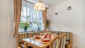 A dining area with a wooden table, striped cushioned seating, and a window with curtains. - Holiday Home 'Storchennest' with Private Terrace, Private Garden and Wi-Fi (Markdorf)