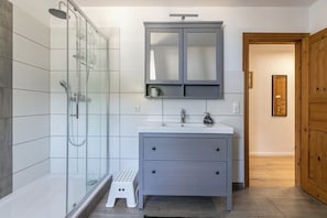 Ein Badezimmer mit Duschkabine aus Glas, einem weißen Waschbecken mit Spiegel darüber und einer Holztür.