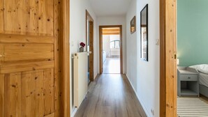 A hallway with wooden doors, a radiator, framed pictures, and a bed in the room.