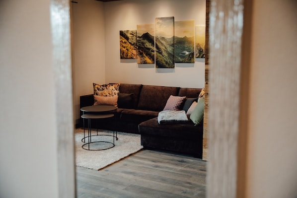 A modern living room with a sectional sofa, a round coffee table, and a large wall-mounted artwork.