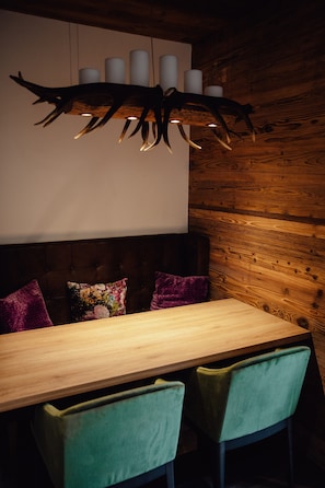 A wooden dining table with two chairs, a wall-mounted light fixture, and a cushion with a floral pattern.