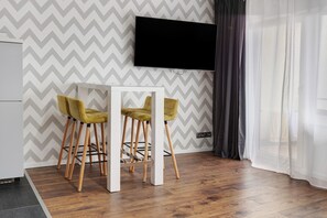 A modern room with a chevron-patterned wall, a flat-screen TV mounted above a white table with two yellow chairs, and a wooden floor. - Studio Apartment 'Ferienwohnung Sally' with Mountain View, Pool and Balcony (Lenzkirch)