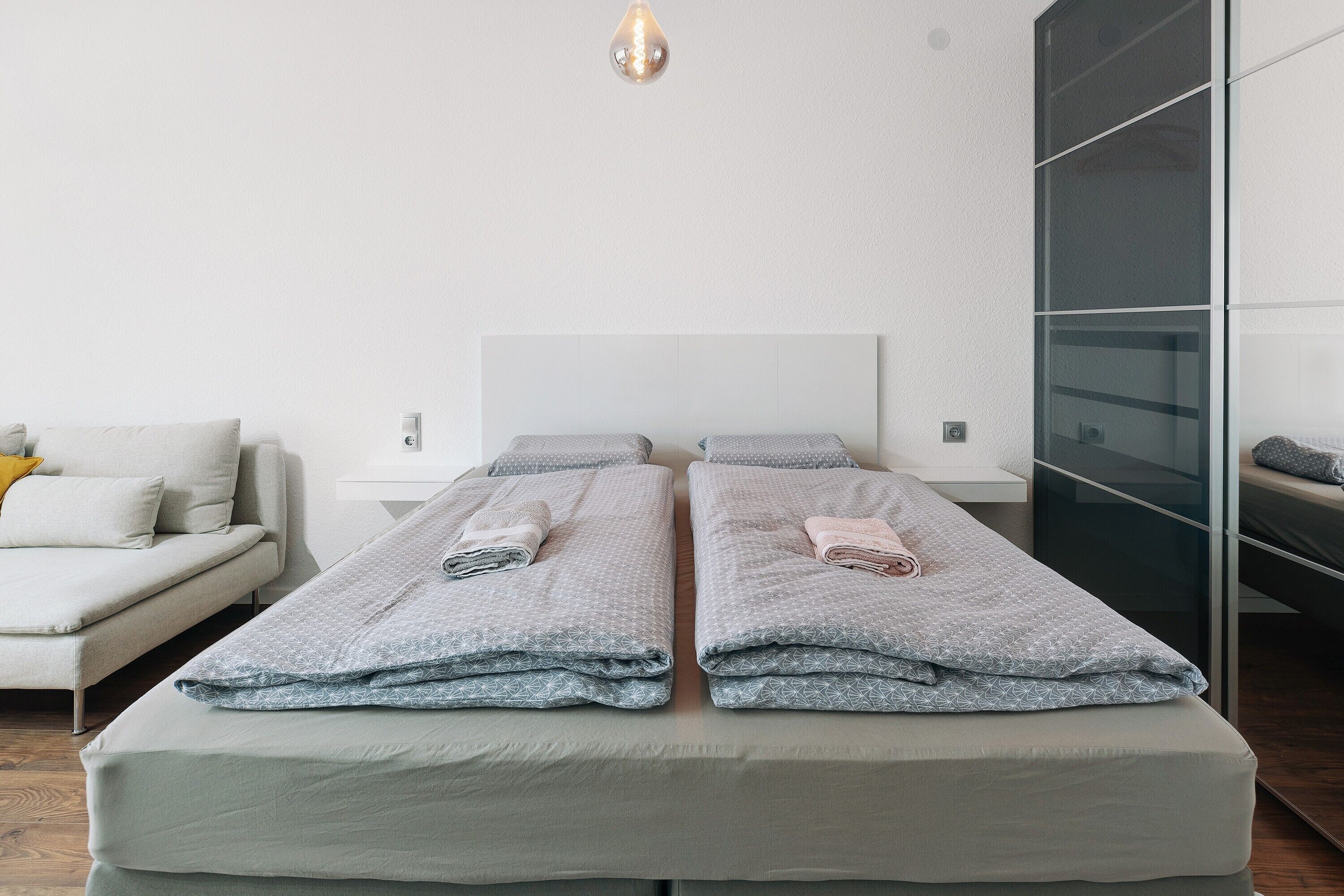A modern hotel room with a large bed, a sofa, and a glass partition wall.