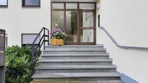 A set of stone steps leading to a door with a glass panel, a small planter with flowers, and a metal handrail. - Studio Apartment 'Ferienwohnung Sally' with Mountain View, Pool and Balcony (Lenzkirch)