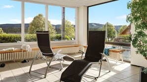 A sunlit room with two reclining chairs, a radiator, and a view of a mountainous landscape through large windows. - Studio Apartment 'Ferienwohnung Sally' with Mountain View, Pool and Balcony (Lenzkirch)