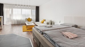 A modern hotel room with a sofa, two beds, a coffee table, and a large window with sheer curtains. - Studio Apartment 'Ferienwohnung Sally' with Mountain View, Pool and Balcony (Lenzkirch)