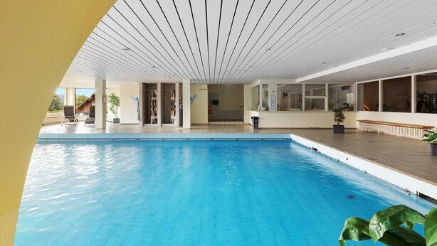 An indoor swimming pool with clear water, a wooden deck, and a bench. - Studio Apartment 'Ferienwohnung Sally' with Mountain View, Pool and Balcony (Lenzkirch)