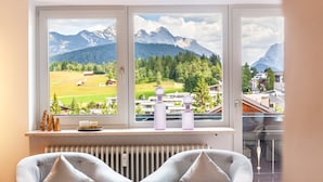 Ein Zimmer mit großem Fenster mit Blick auf eine gebirgige Landschaft, einem Heizkörper und zwei grauen Sesseln.