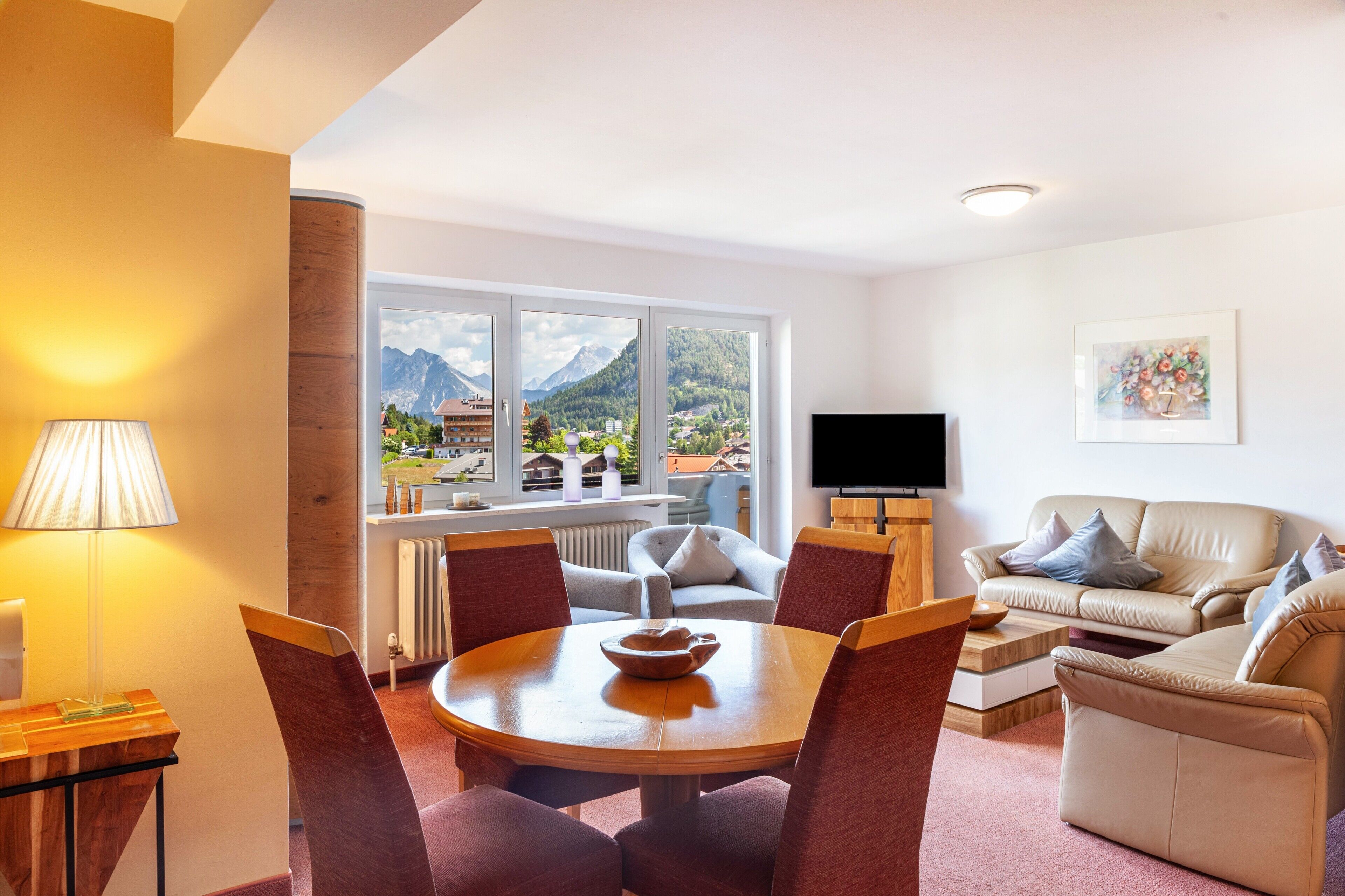 A modern living room with a dining area, a sofa, a TV, and a large window with a mountain view.