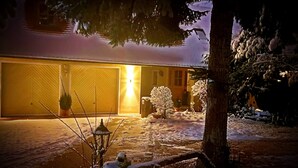 Une allée enneigée menant à un garage dont l’extérieur est éclairé.