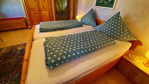 Une chambre à coucher avec un lit en bois, deux oreillers, une table de chevet, un tableau accroché au mur et une armoire en bois.