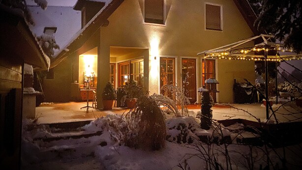 Une maison avec un patio couvert, une cour enneigée et une lumière chaleureuse à l’intérieur.