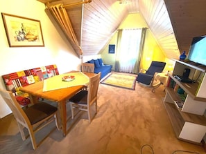 Une pièce mansardée chaleureuse, aménagée avec une table à manger, des chaises, un canapé, un téléviseur et une bibliothèque.