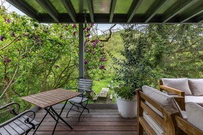 A covered patio with a wooden table and chairs, a sofa, and a potted plant.