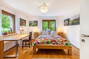 A bedroom with a wooden bed, a desk, a chair, and a window with curtains.