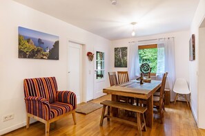A dining area with a wooden table and chairs, a striped armchair, and a view of the outdoors through a window.