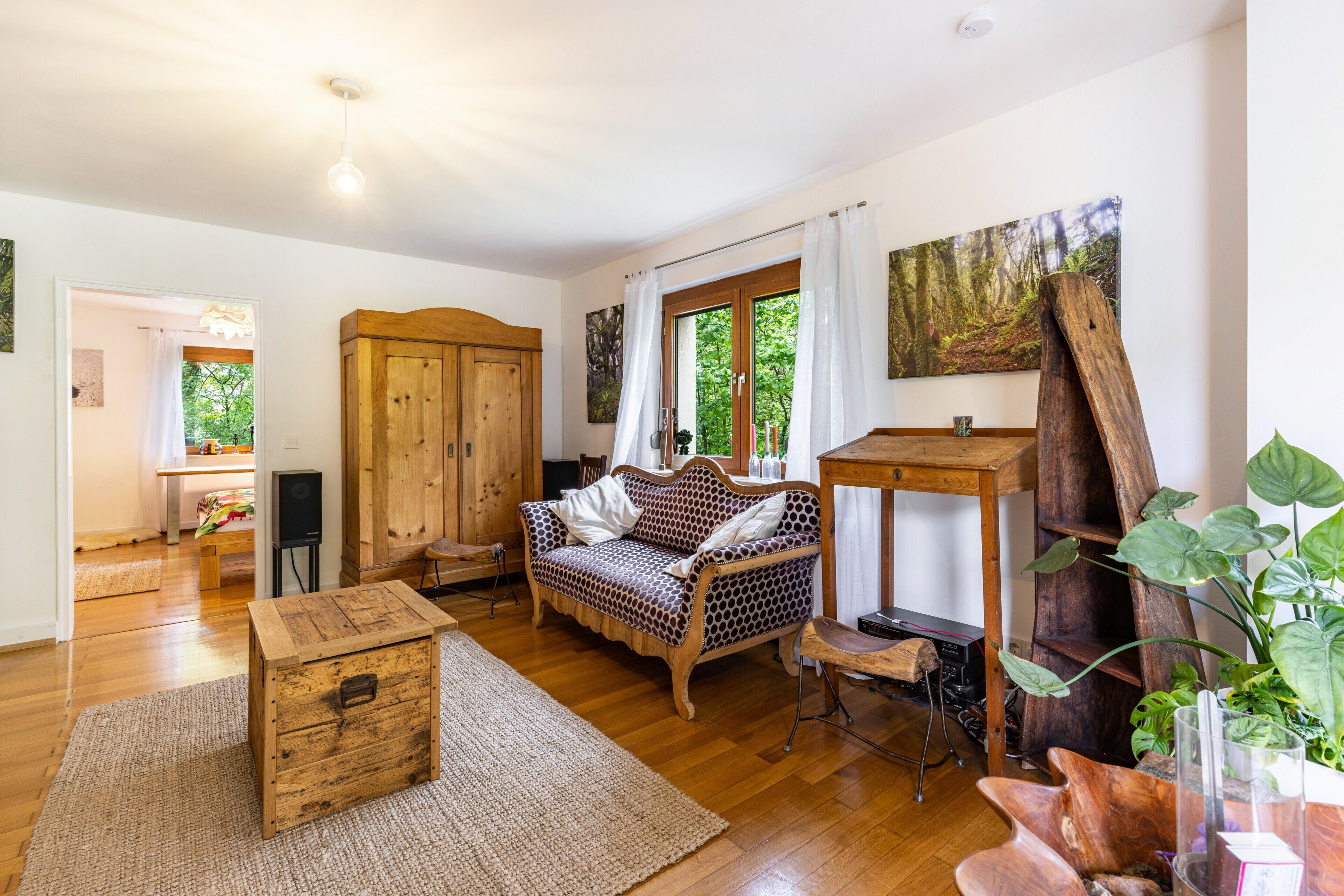 A spacious room with a wooden floor, a sofa, a wooden cabinet, and a large window with curtains.