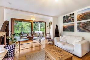 A modern living room with a white sofa, wooden coffee table, and a dining area with a glass door leading to a garden.
