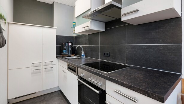 Eine moderne Küche mit weißen Schränken, einer schwarzen Arbeitsplatte und einem eingebauten Backofen.