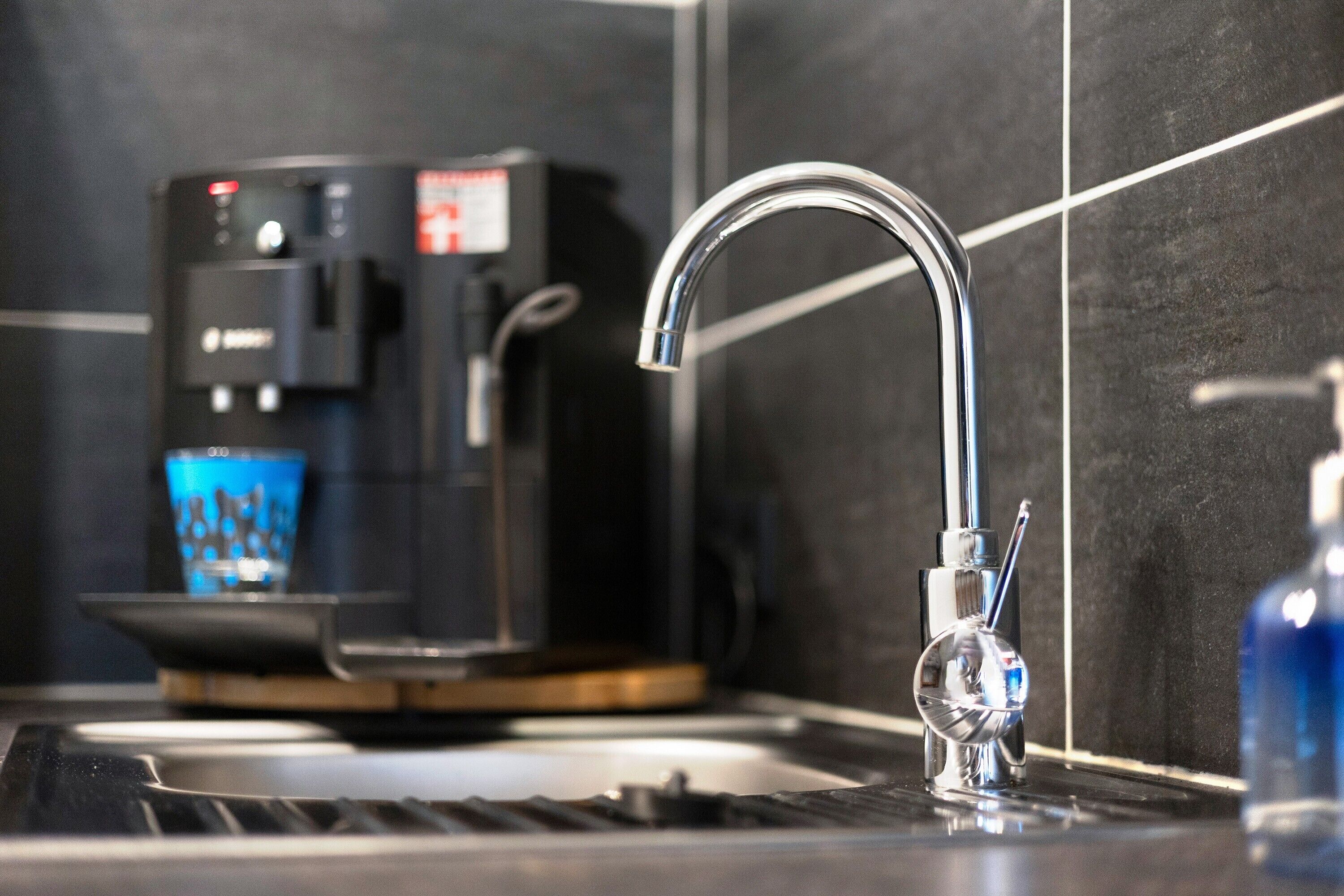 Une cuisine moderne équipée d’un évier en acier inoxydable, d’une machine à café et d’un verre d’eau.