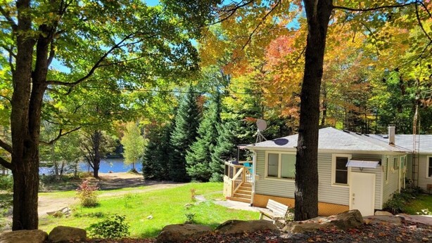 A cabin with a deck, surrounded by trees and a lake. - Cozy Muskoka cottage (Bracebridge)
