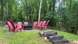 A forested area with red Adirondack chairs and a black fire pit. - Cozy Muskoka cottage (Bracebridge)