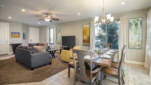 Amplia sala de estar con un sofá gris, un sillón amarillo y un comedor con una mesa de madera preparada para seis personas.
