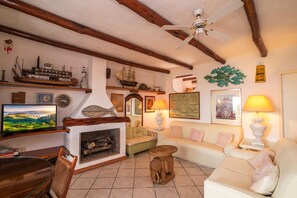 A cozy living room with a fireplace, wooden beams, a television, and various decorative items. - La Perla Del Golfo With Stunning View, Marinella, Italy (Marinella)