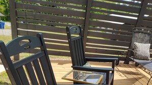 Una terraza de madera con dos mecedoras y una mesita.