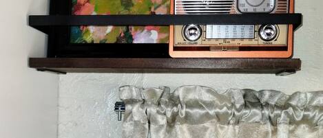 Ein Badezimmer mit Duschvorhang, einem gerahmten Gemälde und einem Vintage-Radio auf einem Regal.