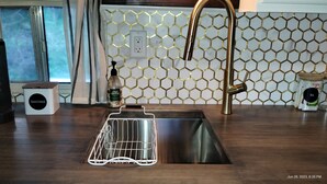 Una cocina con un lavamanos de acero inoxidable, un escurreplatos blanco, una botella de detergente Ever Spring y un backsplash con diseño de panal.