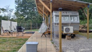 Un espacio al aire libre techado con una autocaravana, una hamaca colgada y una parrilla.