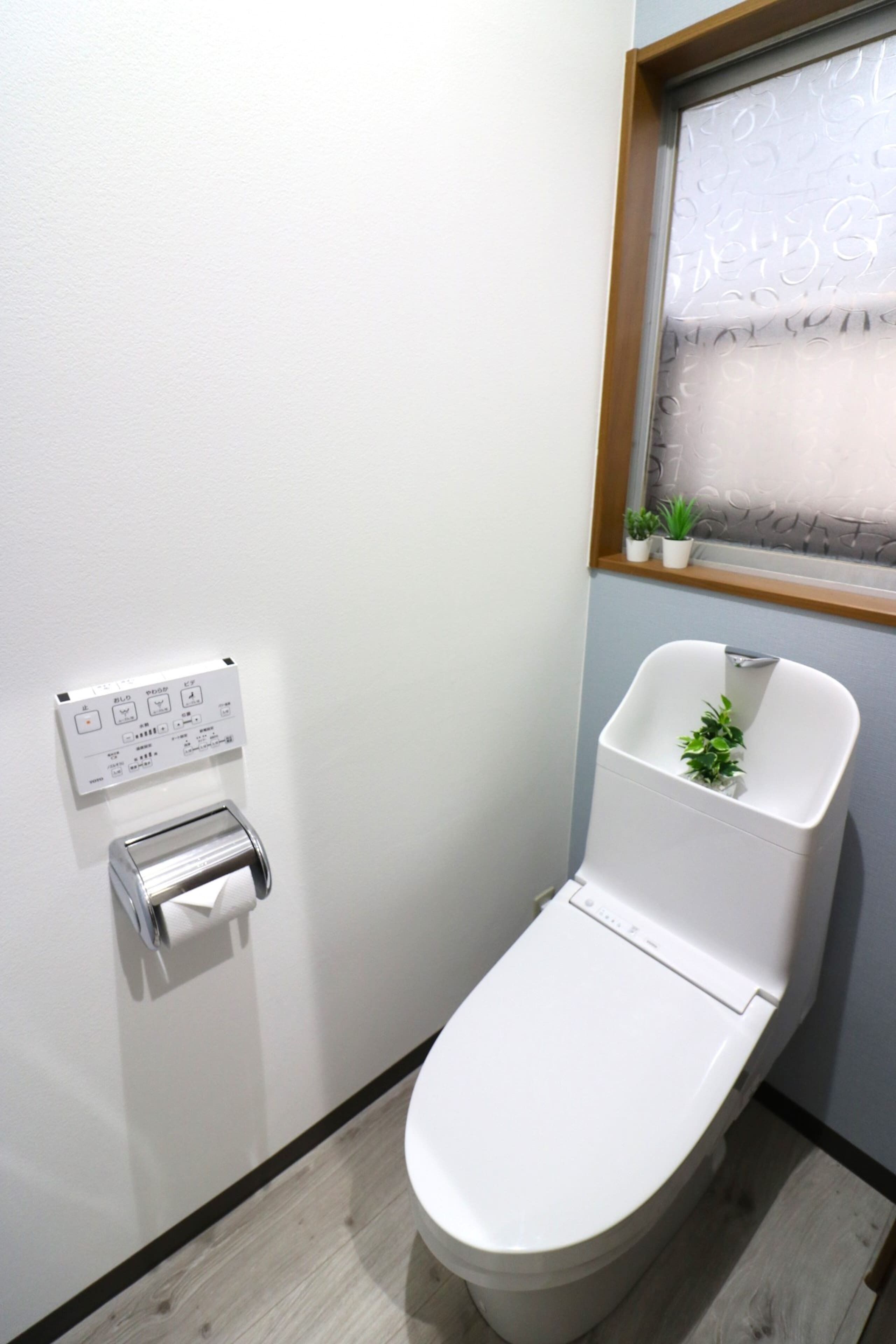 Een moderne badkamer met toilet, handdroger, raam met gezandstraald glas en een kleine plant op de vensterbank.