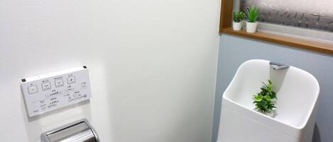 Een moderne badkamer met toilet, handdroger, raam met gezandstraald glas en een kleine plant op de vensterbank.