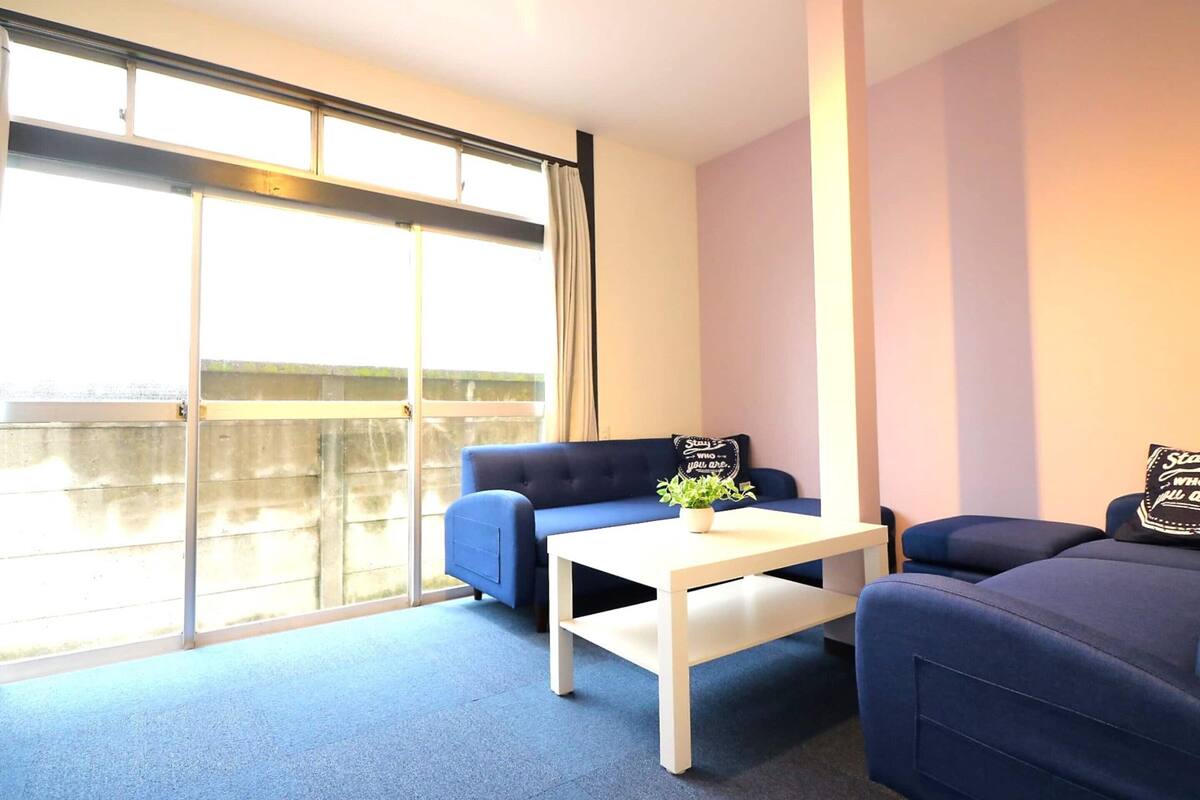 A room with a blue sofa, a white table, and a large window with a view of a building.