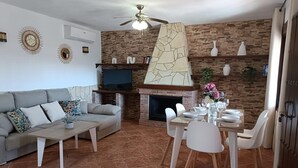 A living room with a sofa, coffee table, TV, fireplace, dining table, chairs, and a ceiling fan.