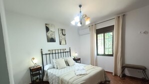 A bedroom with a bed, two bedside tables, a nightstand, a bench, a window with curtains, and wall art.