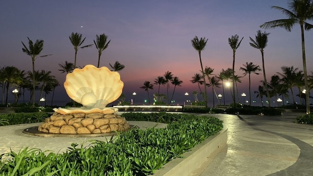 A landscaped area with a large shell sculpture, palm trees, and a pathway. - Minh Anh Hotel (Phu Quoc)