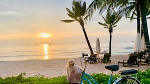 A beach scene with a bicycle parked on the sand, a beach chair, and a small basket on the bike. - Minh Anh Hotel (Phu Quoc)
