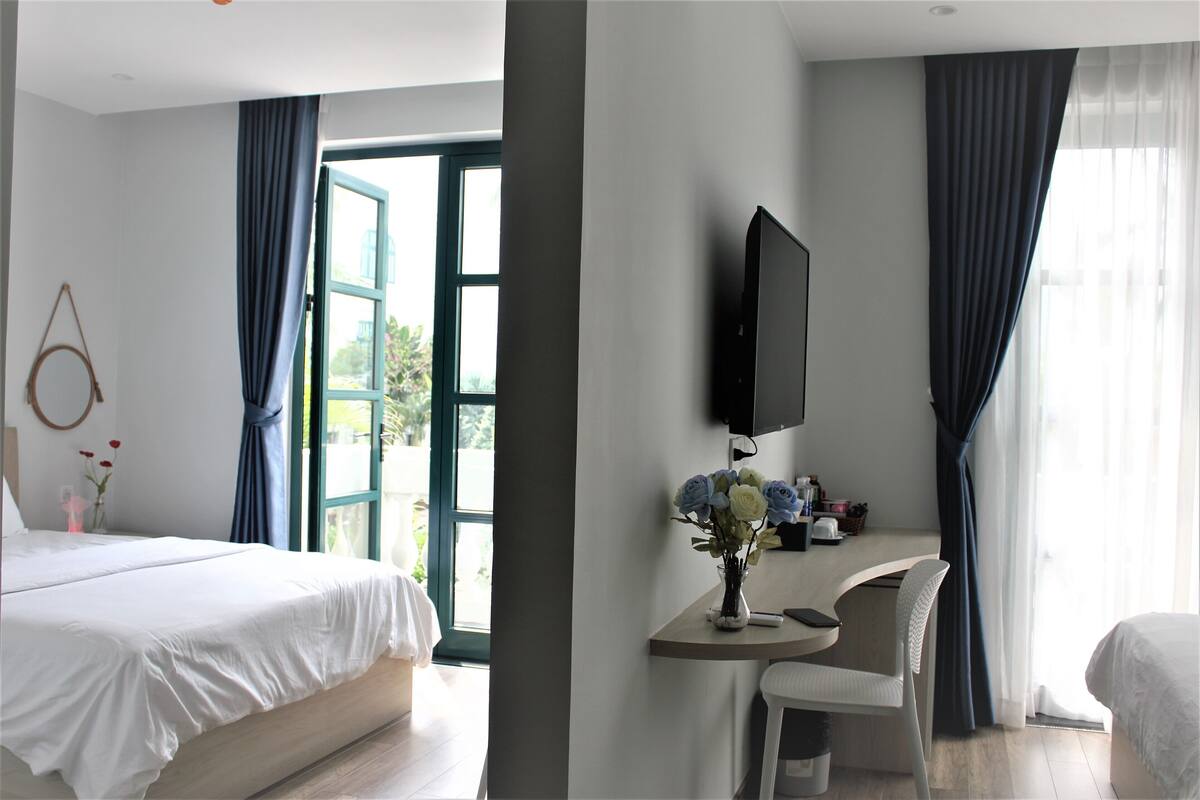 A hotel room with a bed, a desk with a chair, a TV, and a window with curtains.