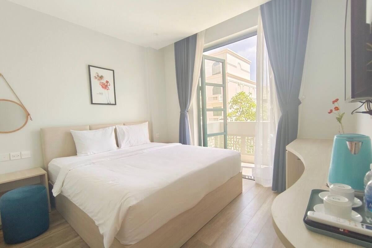 A hotel room with a large bed, a small desk, a coffee maker, and a view of the outside.