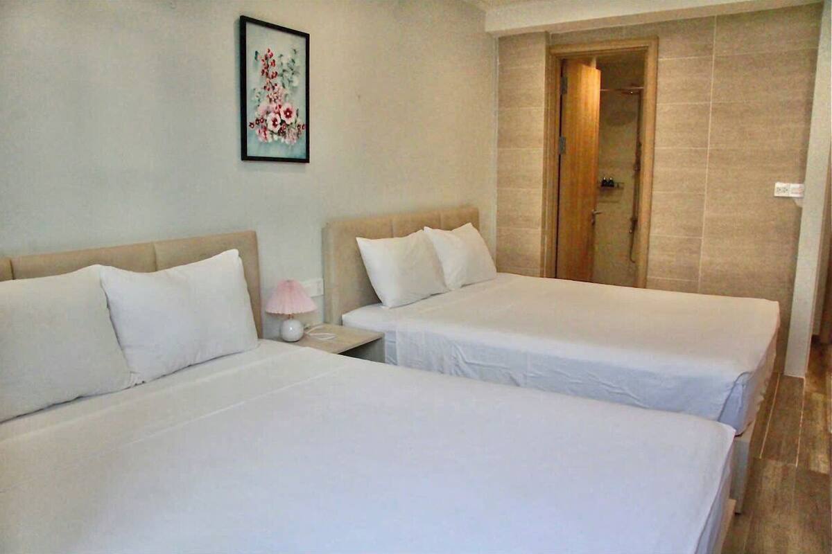 A hotel room with two beds, a nightstand with a lamp, and a shower area.