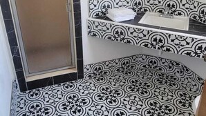A bathroom with black and white patterned tiles, a mirror, and a towel rack. - Wiebe Motel (Hollister)
