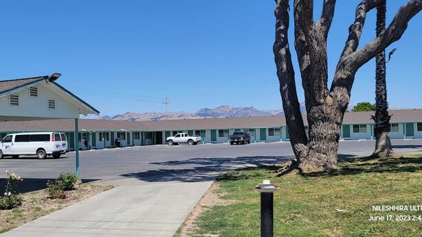 A motel with a covered parking area, a row of motel rooms, and a mountain view in the background. - Wiebe Motel (Hollister)